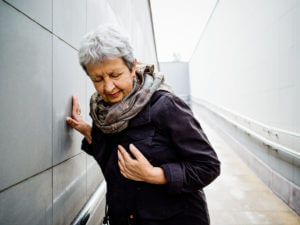 An older woman walking outside while she clutches her chest and looks confused as she is experiencing symptoms of a seizure.