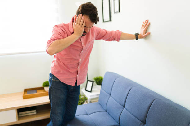 Disoriented man in his 30s feeling dizzy and trying to balance against a wall background. Sick man with vertigo illness