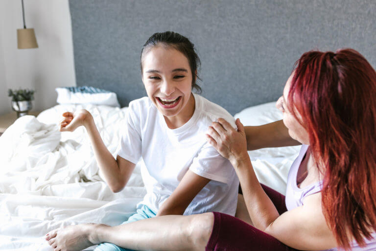 Latin mom and teenage daughter with cerebral palsy having fun on bed at home,