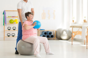 Older woman sitting on a yoga ball doing physical therapy exercises as part of her Parkinson's disease treatment plan.